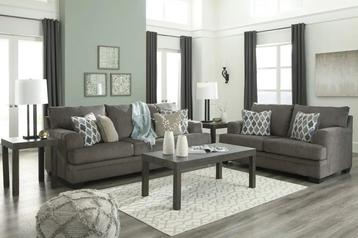 Plush textured gray loveseat and sofa set with corner-blocked frame. Attached back and loose seat cushions filled with high-resiliency foam wrapped in thick poly fiber for comfort. Includes two decorative pillows in blue, brown, and tan with soft polyfill. Upholstered in polyester fabric, with exposed feet featuring a faux wood finish. Platform foundation system provides even support and maintains a tight, wrinkle-free look.
