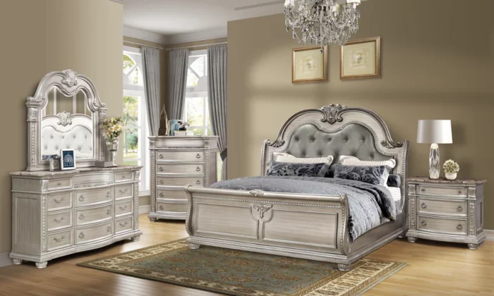 B9506 6 Piece Bedroom Set in antique platinum finish with plush tufted headboard set against a silver backdrop, ornate carvings, and marble tops on dresser and nightstands.